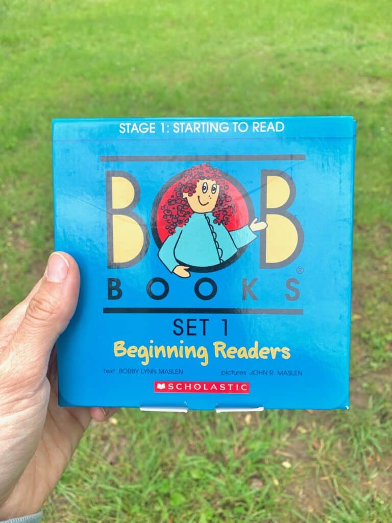 A hand holding the blue box from the BOB Books beginning reader series