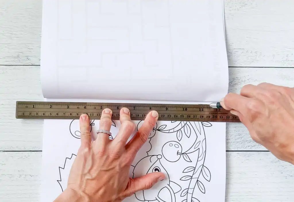 Hands using a hobby knife to cut along a metal ruler in order to remove a page from a coloring book