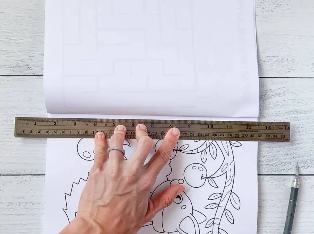 A hadn't holding a metal ruler along the margin of a fox coloring page in a book