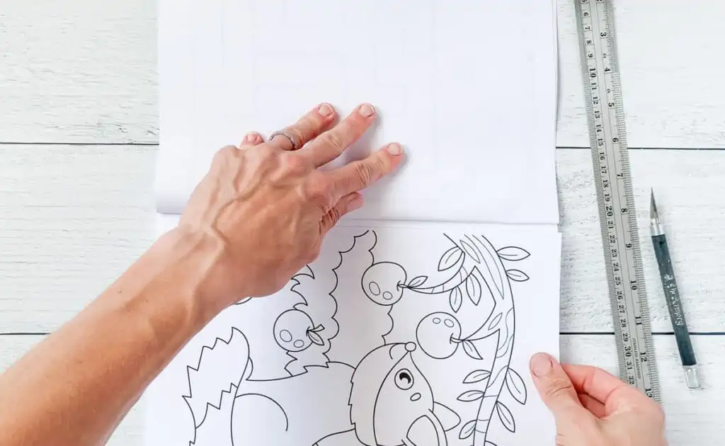 Hands removing a cut coloring book page from a book