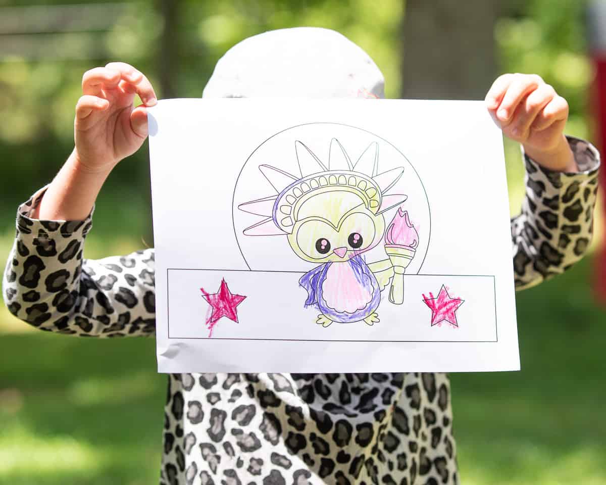 A child holding a colored fourth of july headband craft page in front of her face
