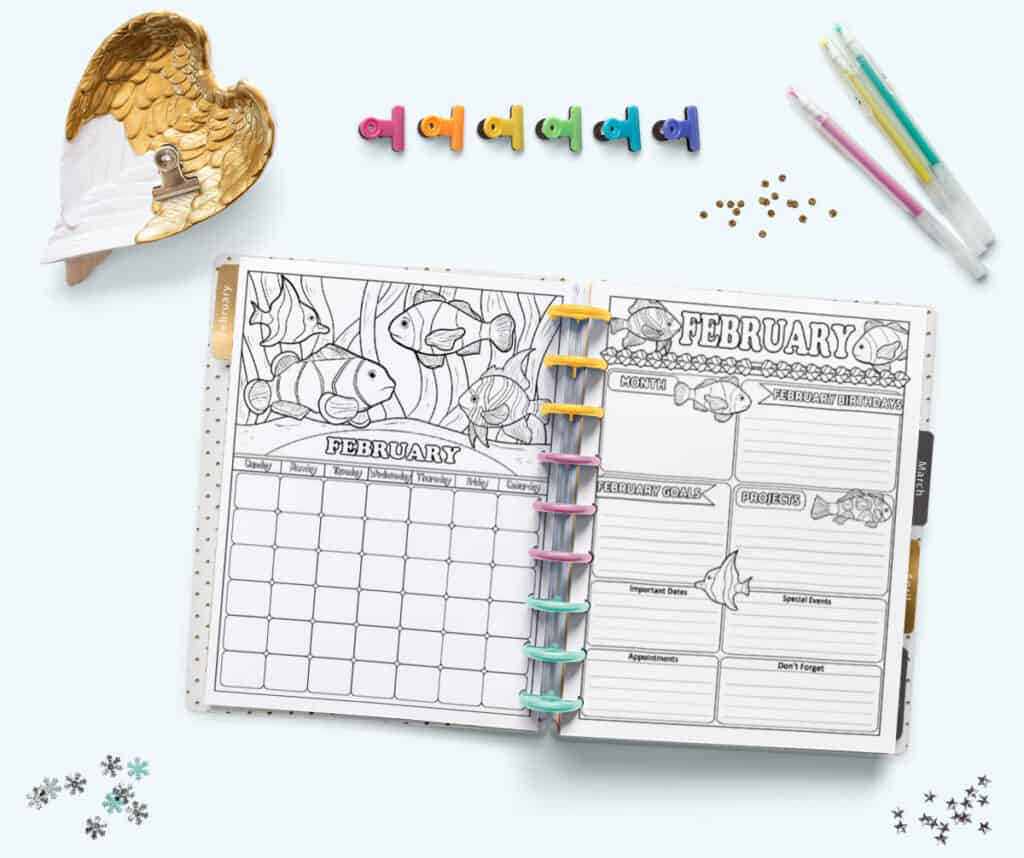 An open Happy Planner Classic with multicolored rings showing a monthly calendar page and planner page for February. The pages are undated and have clownfish to color.