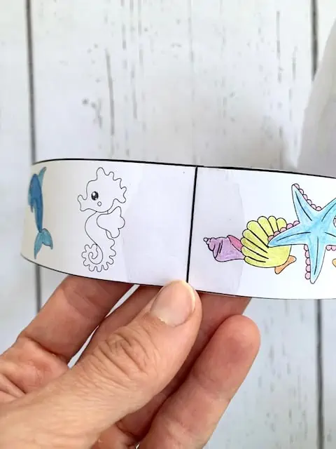 Taping together the pieces of a printable headband craft to make a mermaid crown.