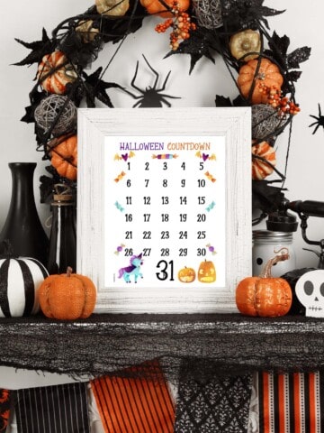 A preview of a Halloween countdown calendar in a white picture frame on a mantle decorated for Halloween