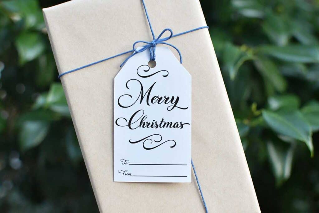 A gift tag with "Merry Christmas" in calligraphy attached to a brown paper wrapped package