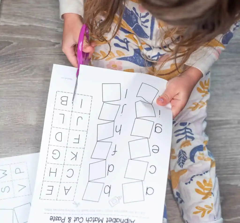 An image of a young child using blunt-tipped scissors to cut out letter tiles
