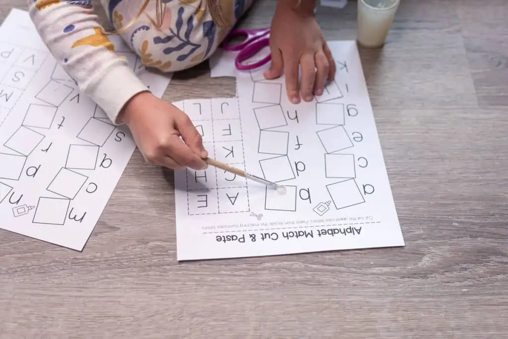 A pre-k aged child using a paintbrush to glue an uppercase letter tile next to its lowercase counterpart