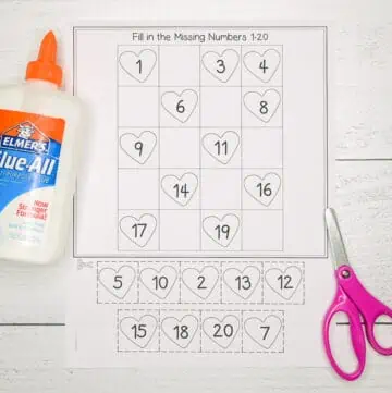 A cut and paste fill in the missing numbers 1-20 worksheet for Valentine's Day. It is shown with a pair of scissors and bottle of glue.