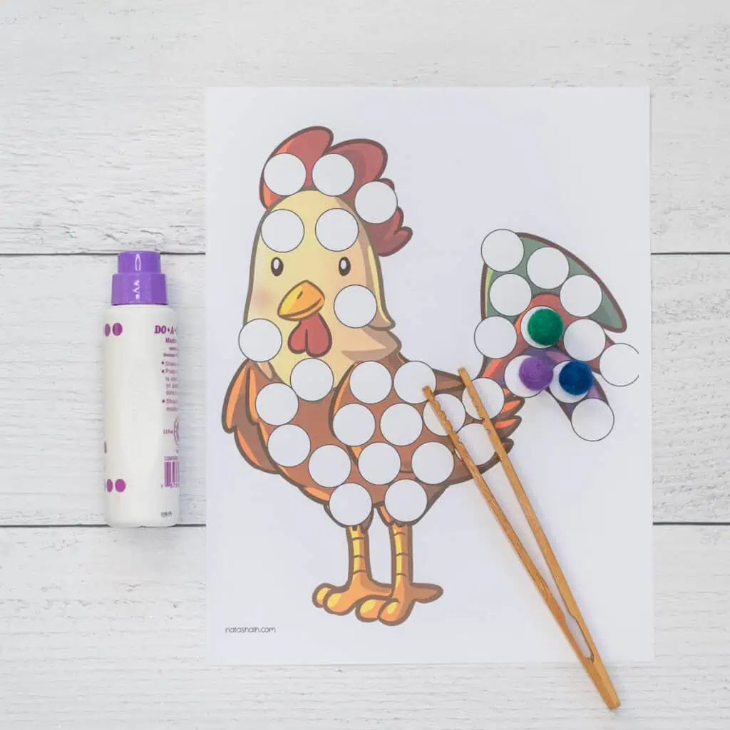 A rooster dot marker coloring page shown with a purple dab it marker, pom pops, and bamboo tongs.