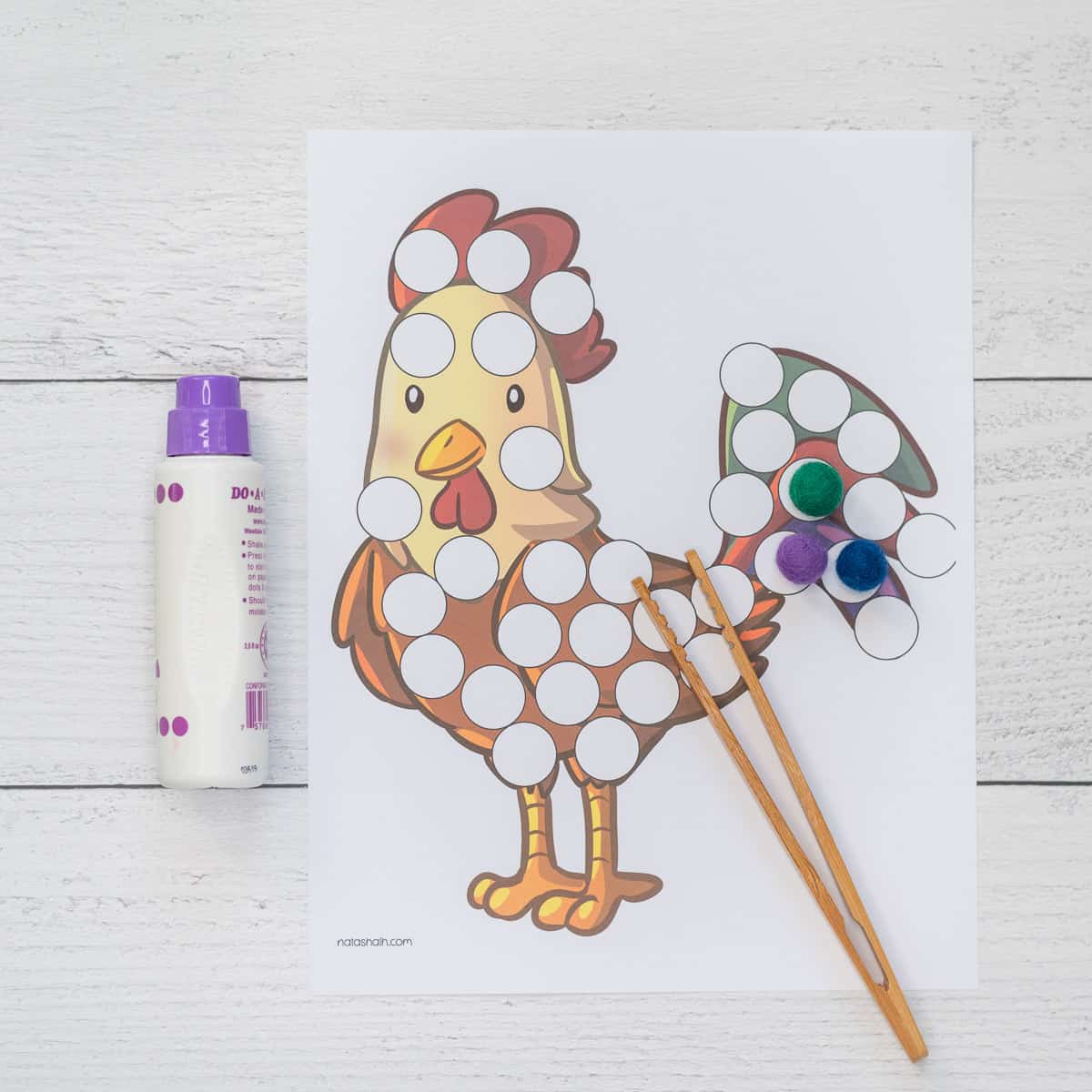 A rooster dot marker coloring page shown with a purple dab it marker, pom pops, and bamboo tongs.