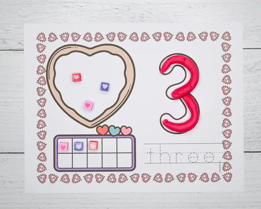 A number three Valentine's play dough number mat with pink play dough on the 3 and heart beads on the ten frame