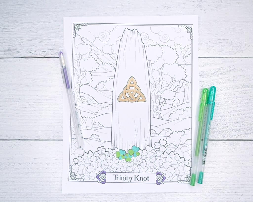 A partially colored coloring page with a trinity knot. It is shown with two green gel pens and one purple gen pen.