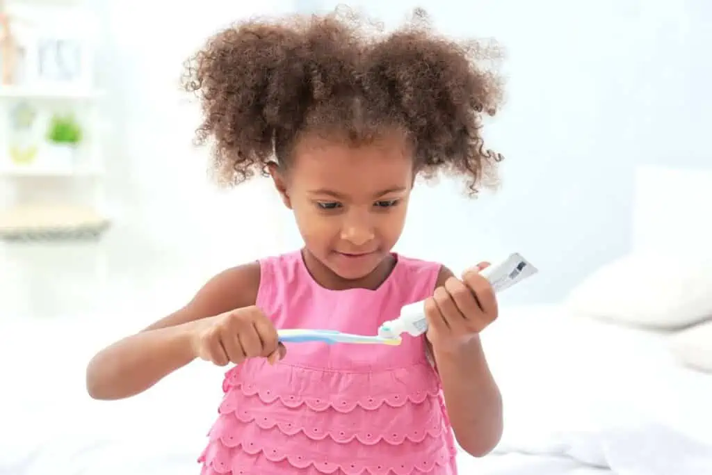 A young girl putting toothpaste one a toothbrush 