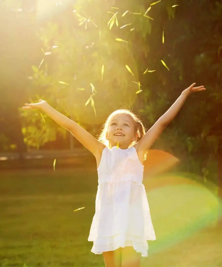 A happy young girl standing with arms raised in the sun