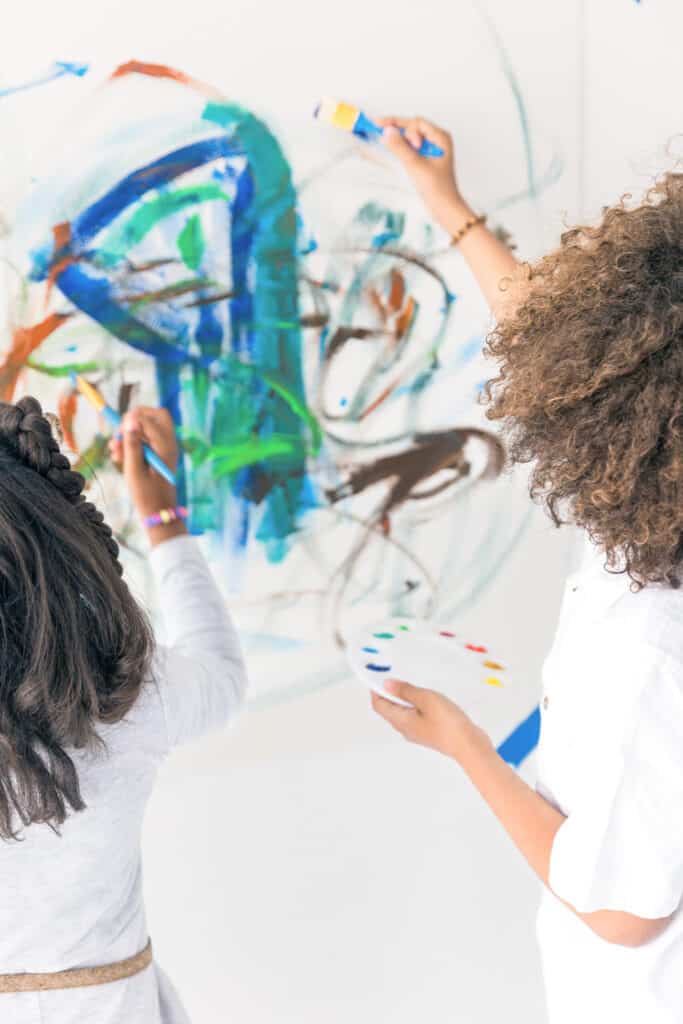 Two children painting a colorful, abstract painting on a wall