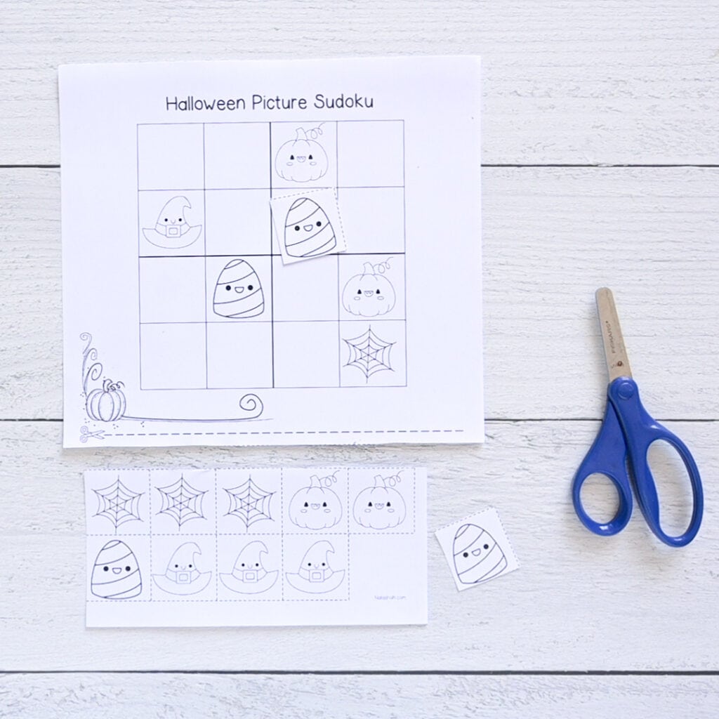 A top down image of using a child's cut and paste Halloween picture Sudoku printable. It is shown with two tiles cut out and a pair of children's scissors.