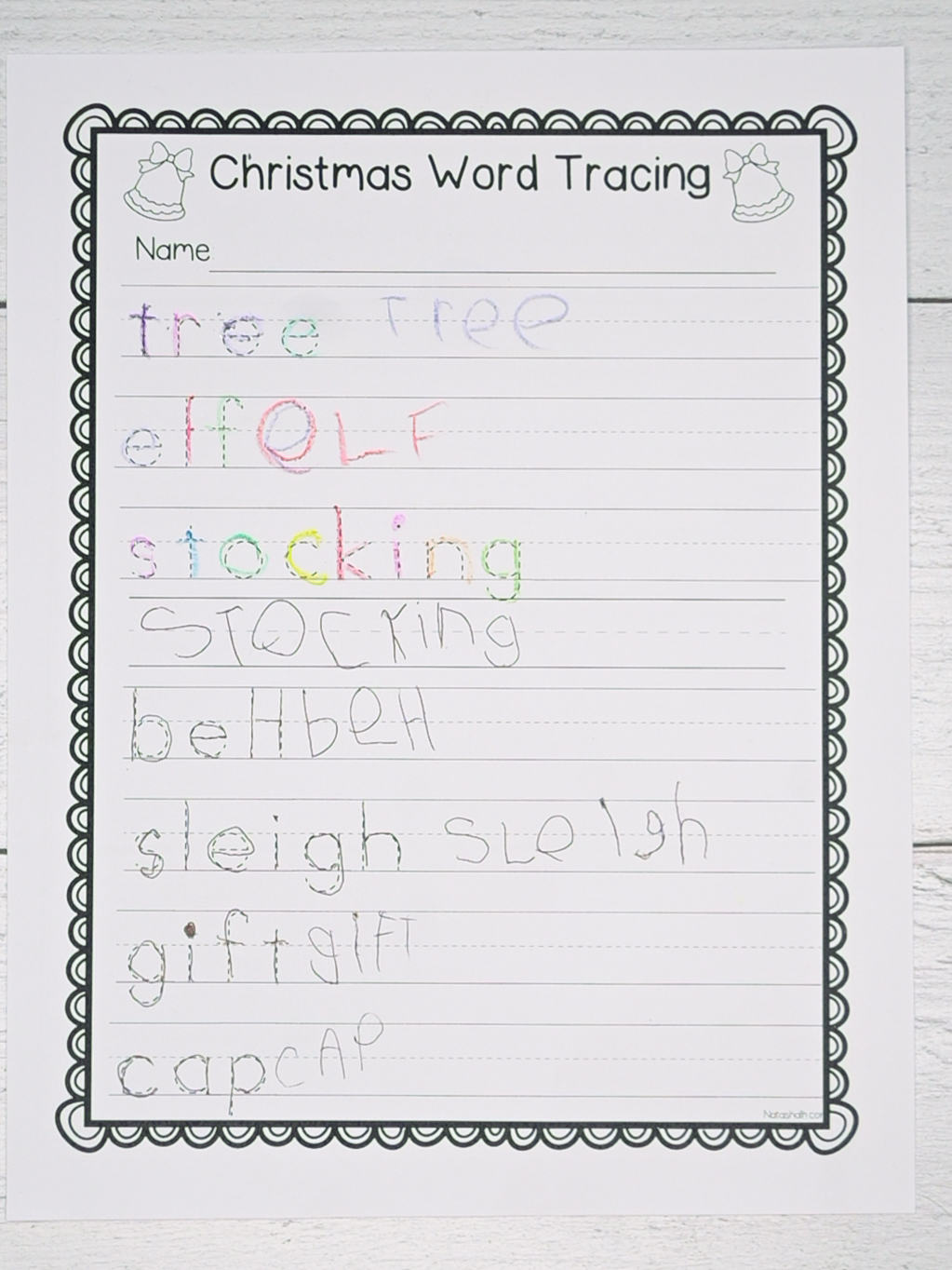 A top down photograph of a christmas word tracing worksheet that has been completed by a kindergarten student