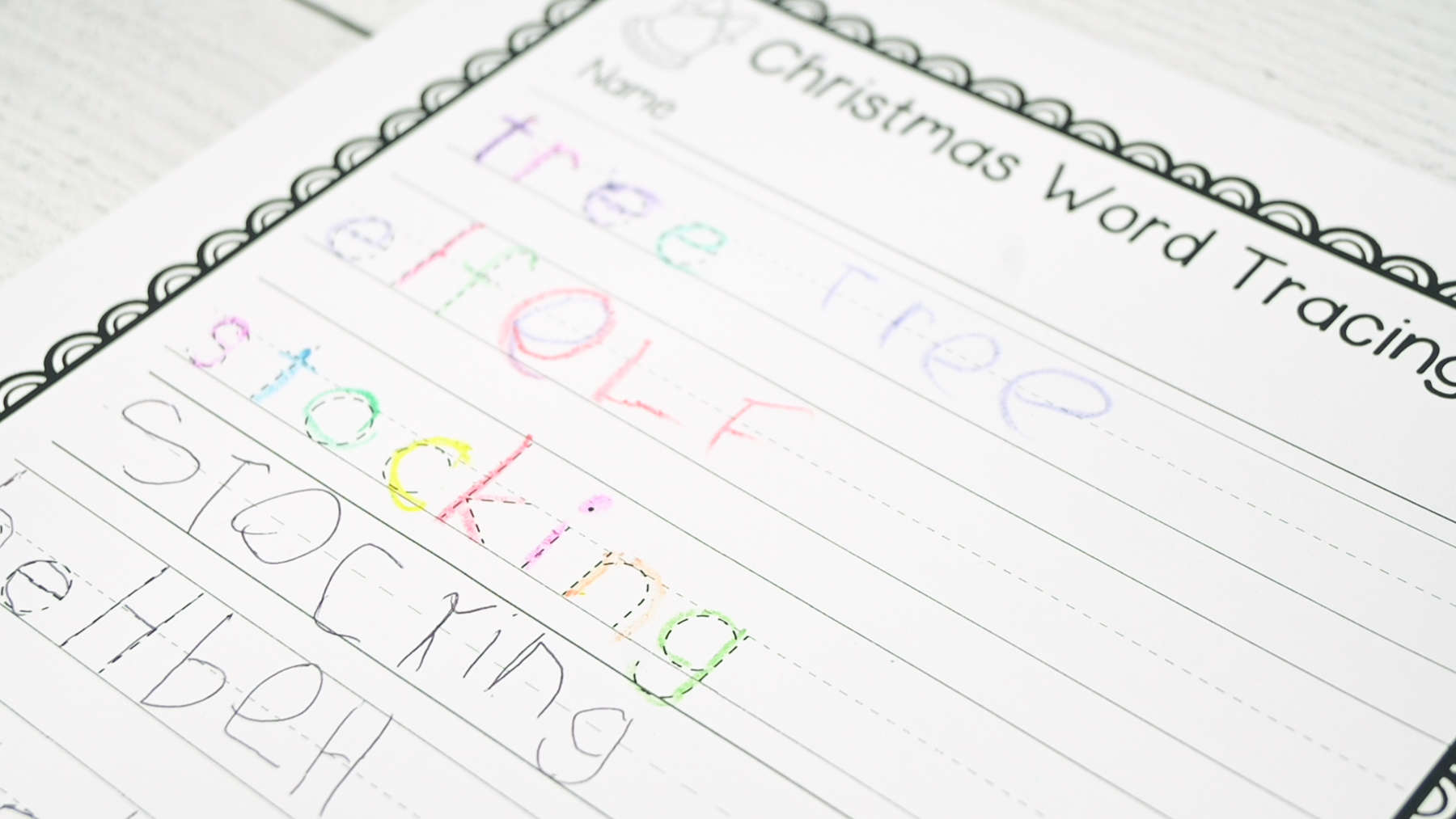 a photograph of a Christmas word tracing worksheet that has been completed by a kindergarten student who traced each letter in a different color