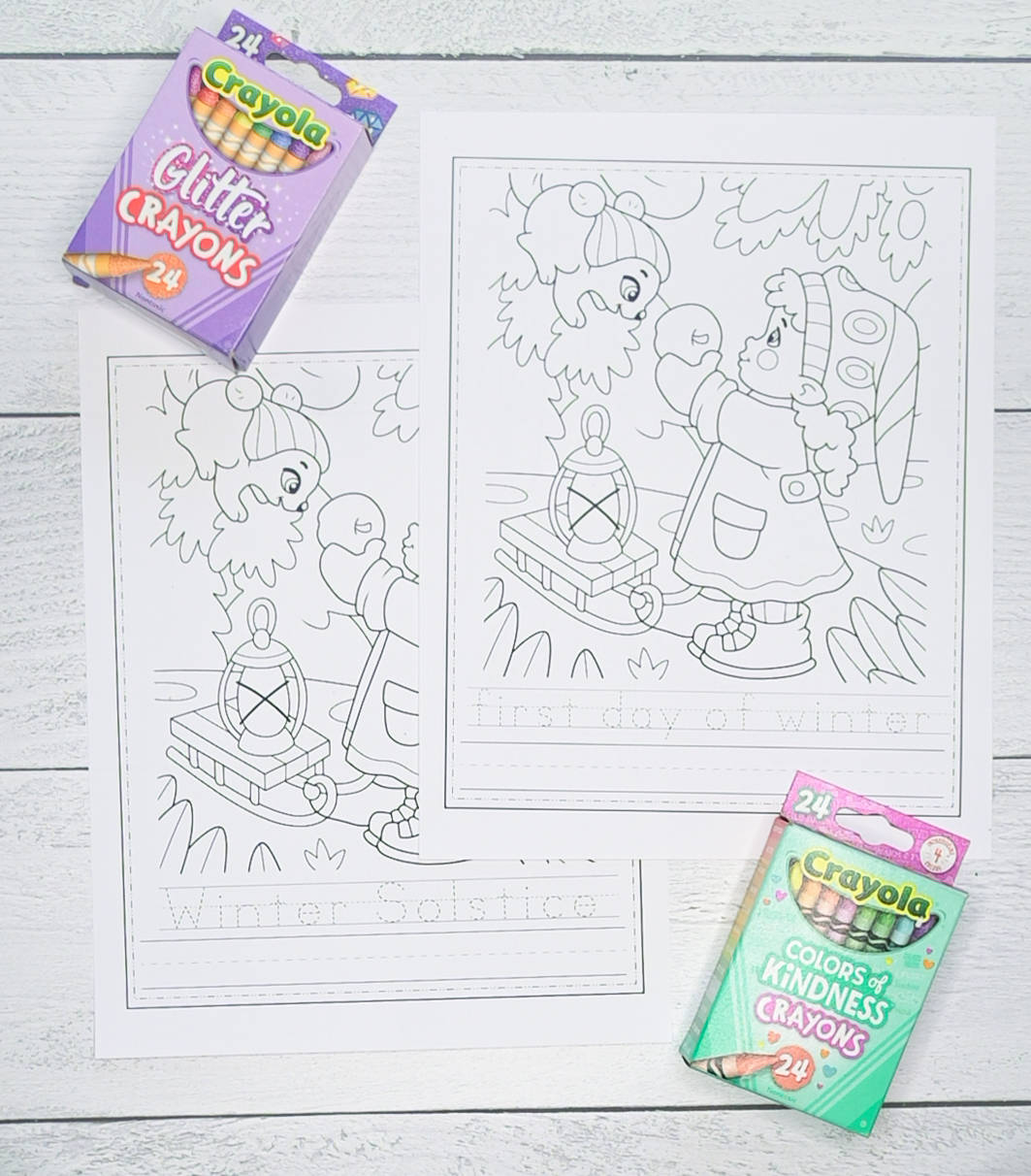 A top down photo of two printable worksheets. Each worksheet has a winter scene to color and words to trade. One says "first day of winter" and the other "Winter Solstice." The pages are shown with two boxes of crayons.