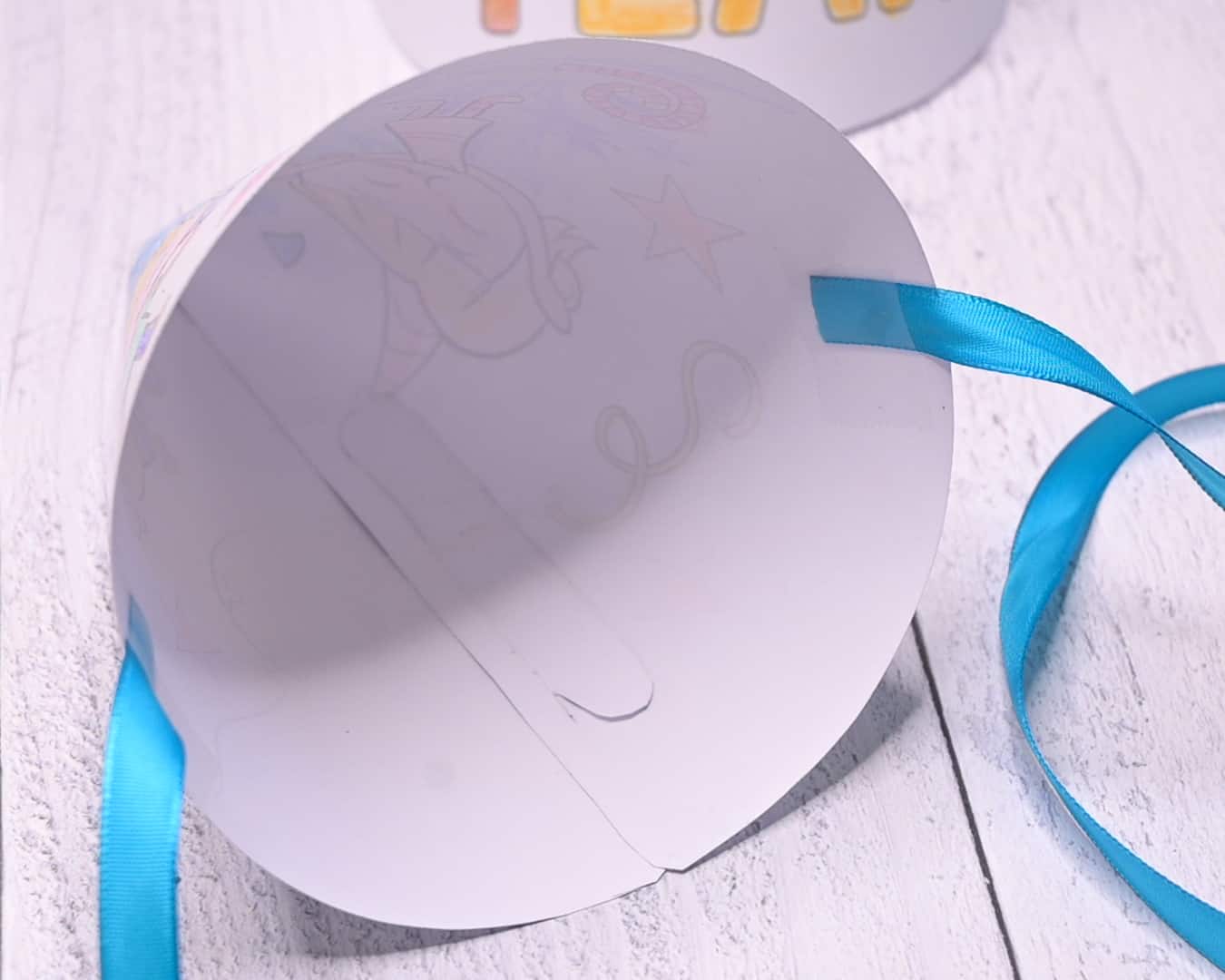 The inside of a printable party hat with blue ribbons taped to hold the hat in place