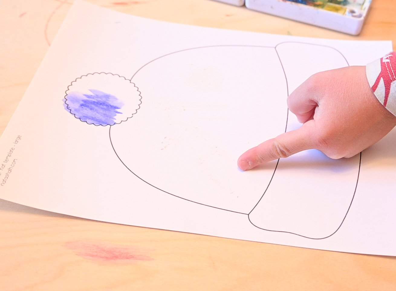 A child's finger pointing at a drawing made in white crayon on a printable hat template