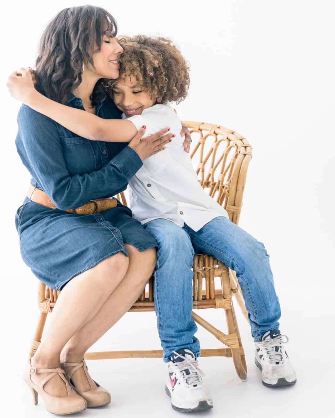 A photo of a mom in a denim dress hugging her son.