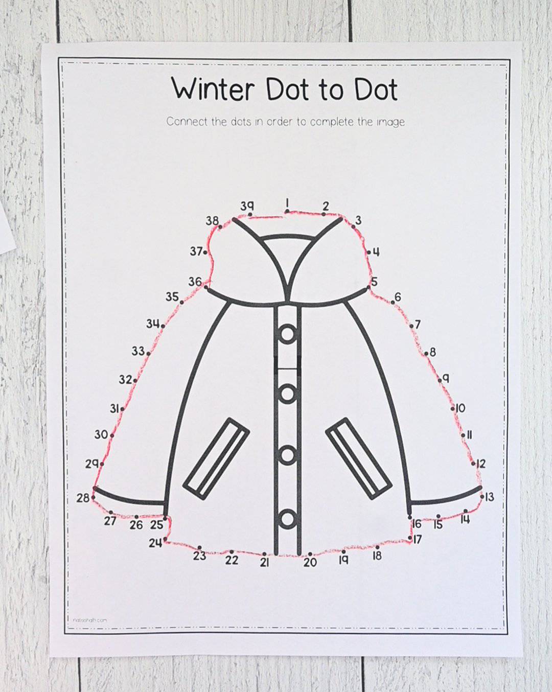 A top down picture of an easy dot to dot image of a coat that has been completed with red crayon