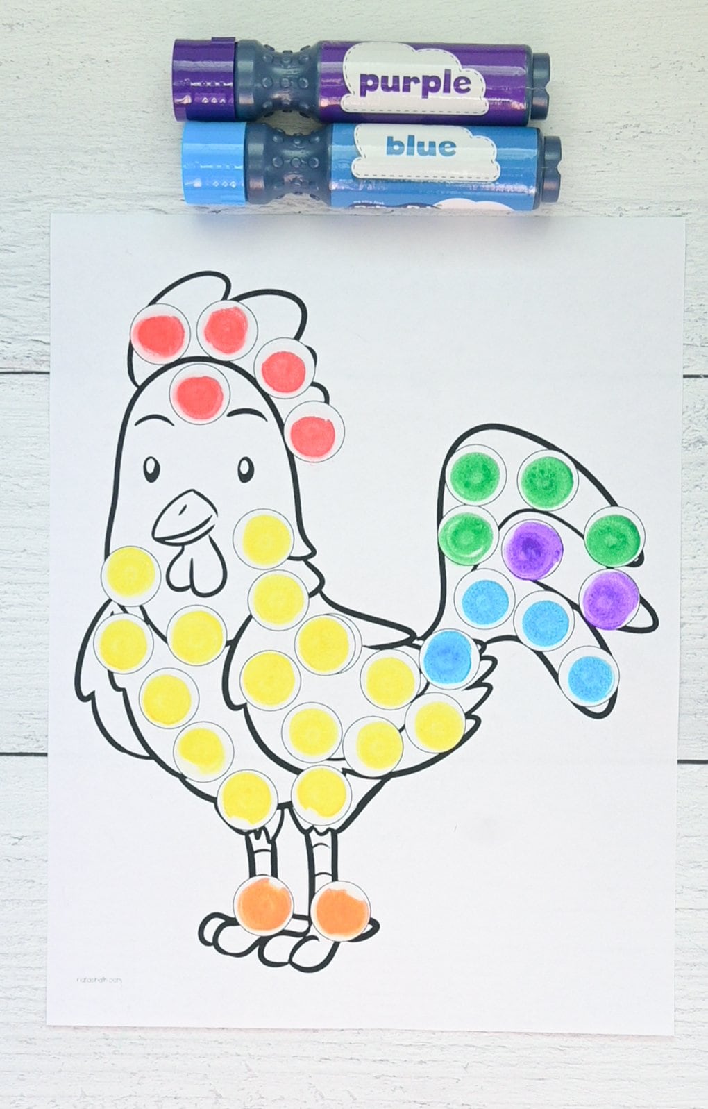 A top down photo of a completed rooster dot marker coloring page with a purple dot marker and a blue dot marker