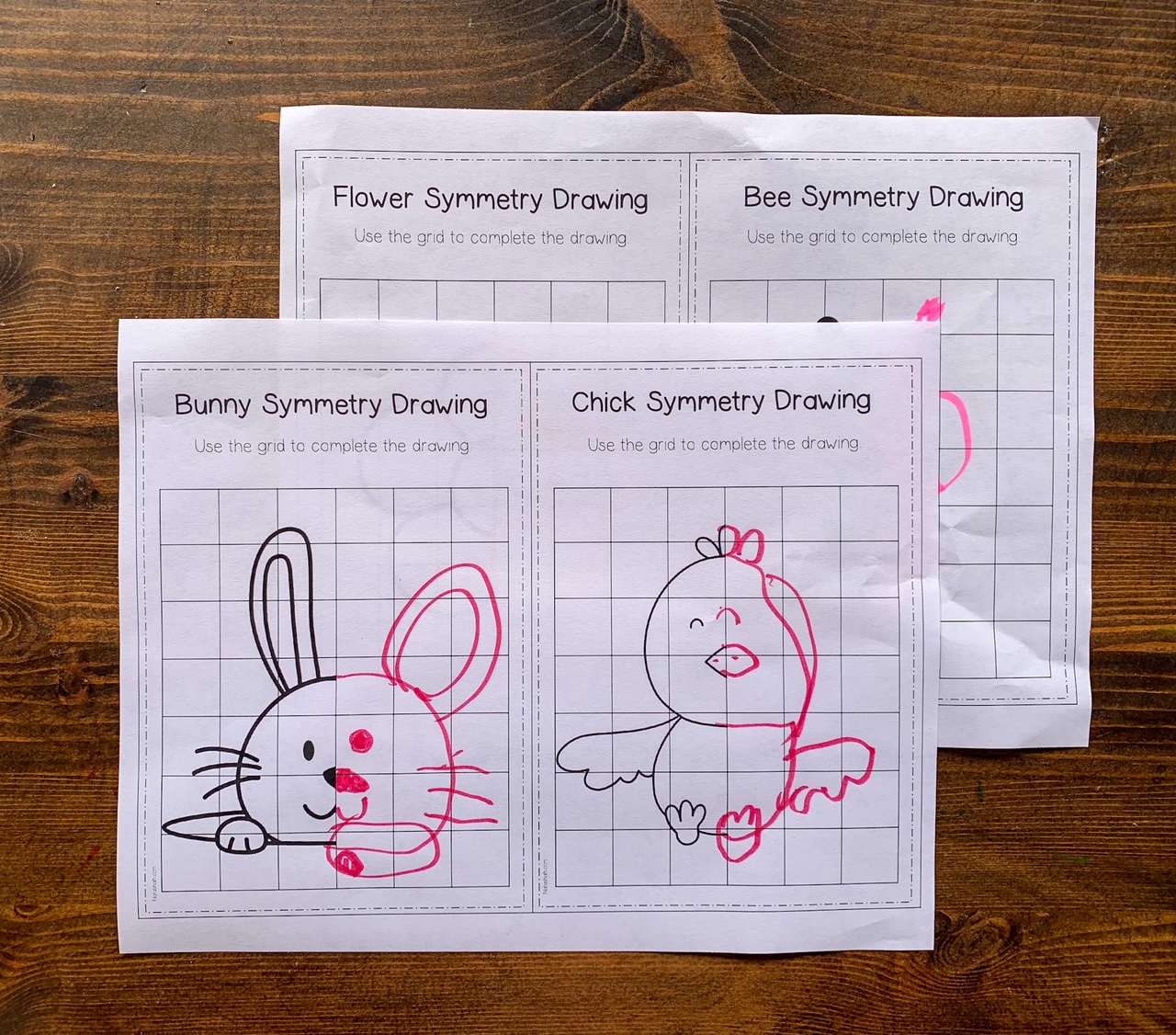 A photo of two pages of completed spring themed symmetry drawing cards. The front page has a bunny and a chick.
