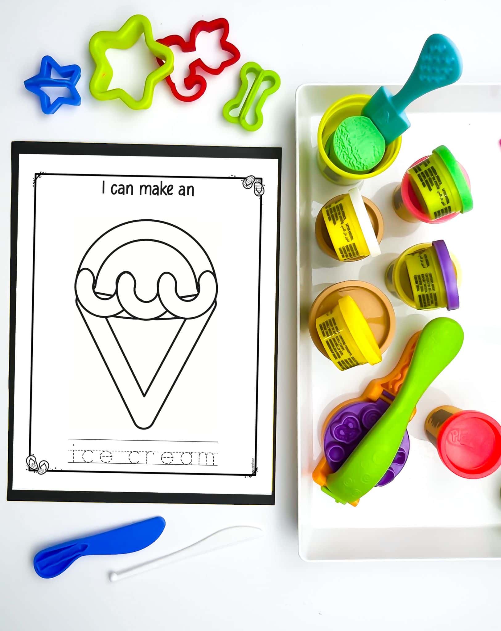 A top down photo of an ice cream themed play dough activity mat printable net to a tray with play dough containers and tools