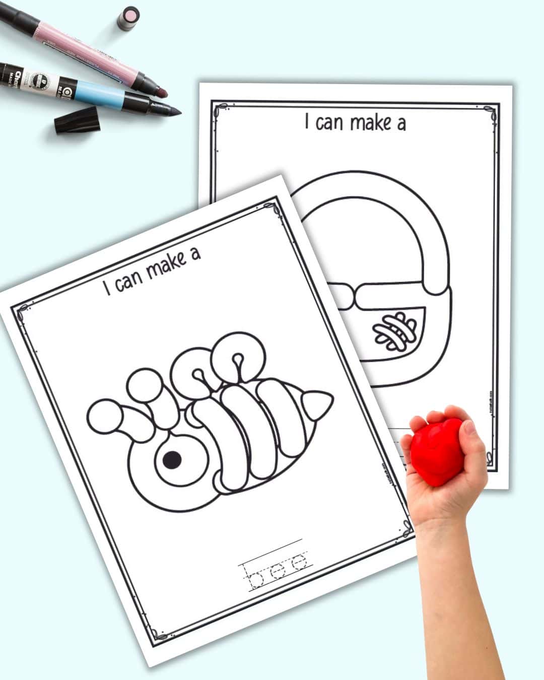 Two black and white play dough mats. One shows a bee and the other a basket. A child's hand holding a ball of red play dough is also in the frame