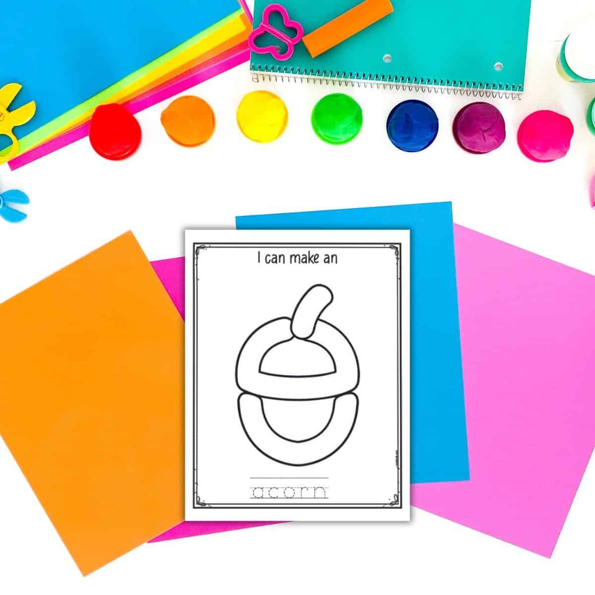A top down photo of play dough and colorful papers with a printable acorn play dough mat in black and white