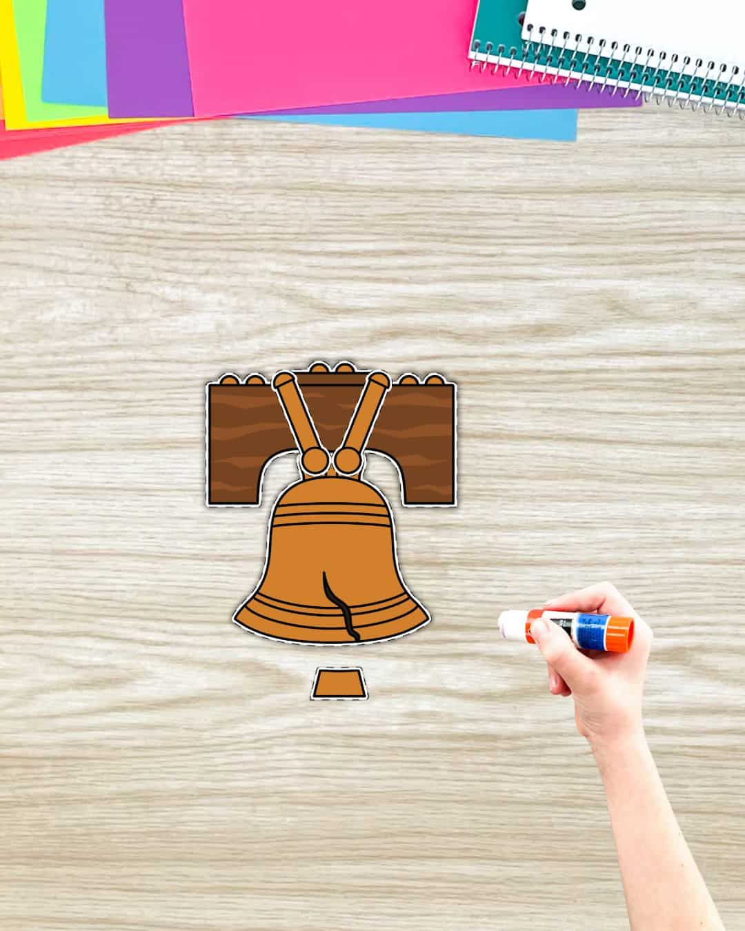 A Liberty Bell cut and paste craft being made with a hand holding a glue stick