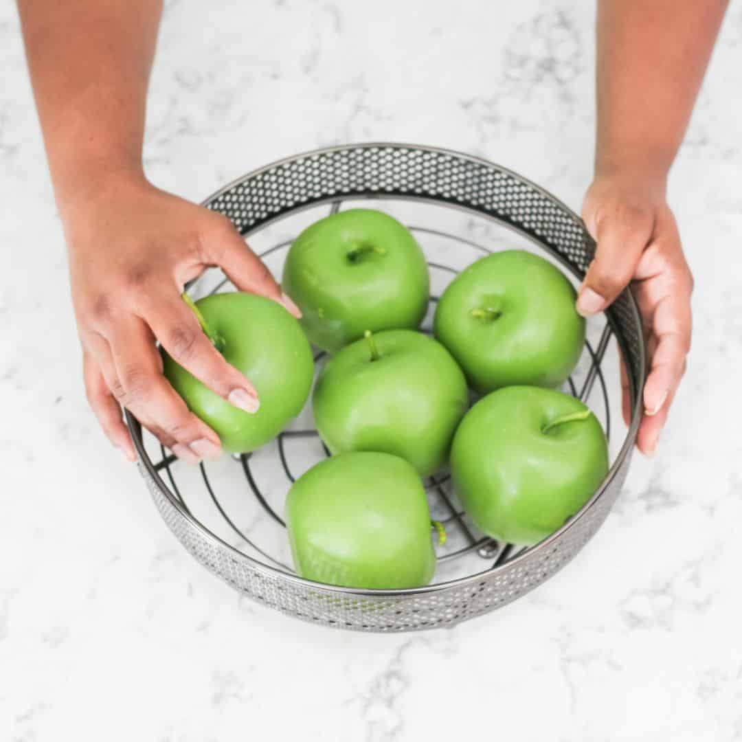 Hands picking a green apple out of a bowl