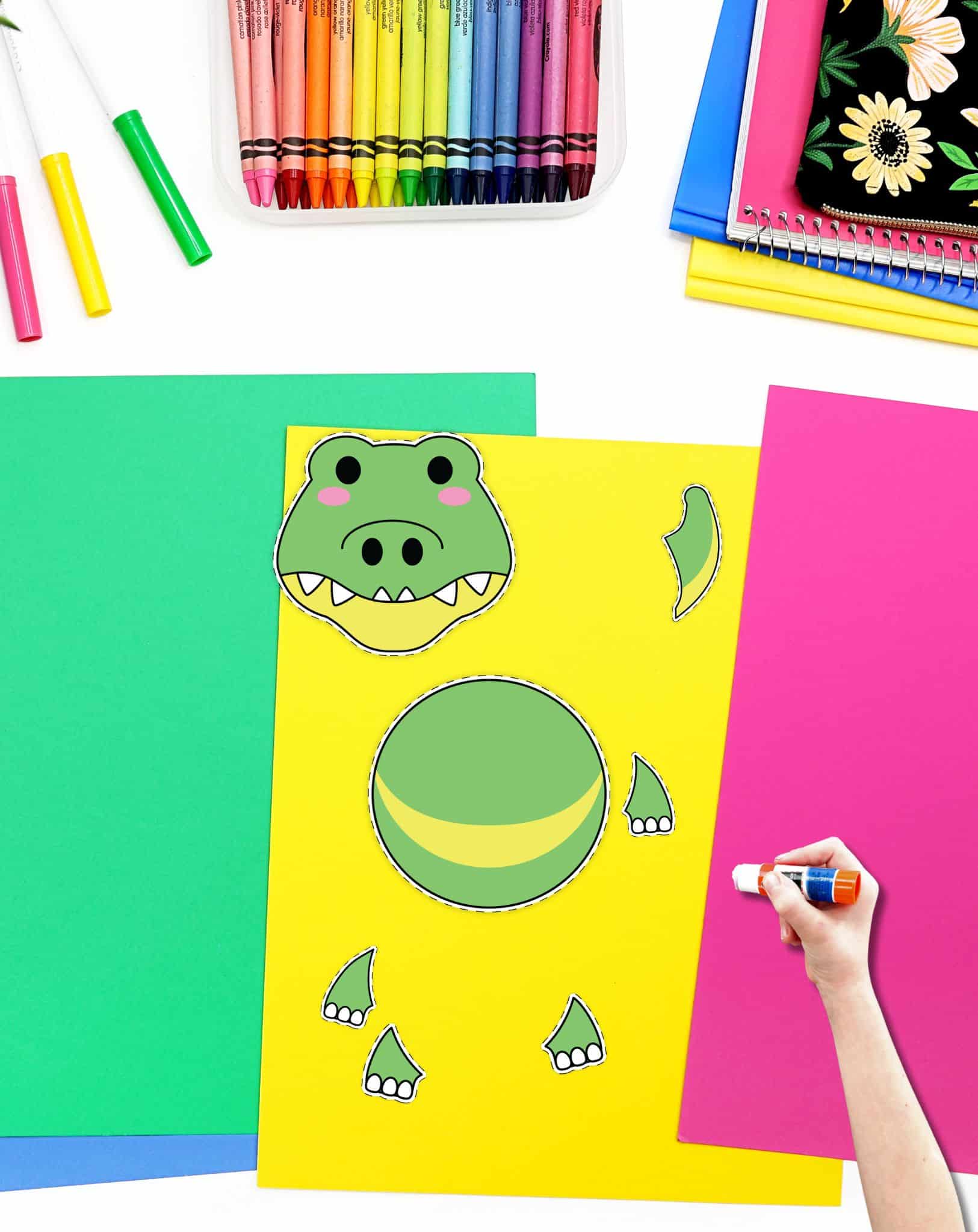 Cut out pieces for an alligator craft on a desk with colorful papers and crayons