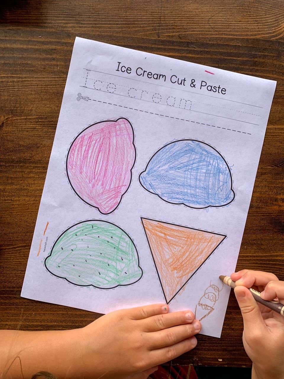 A child's hand coloring a printable cut and paste ice cream craft 