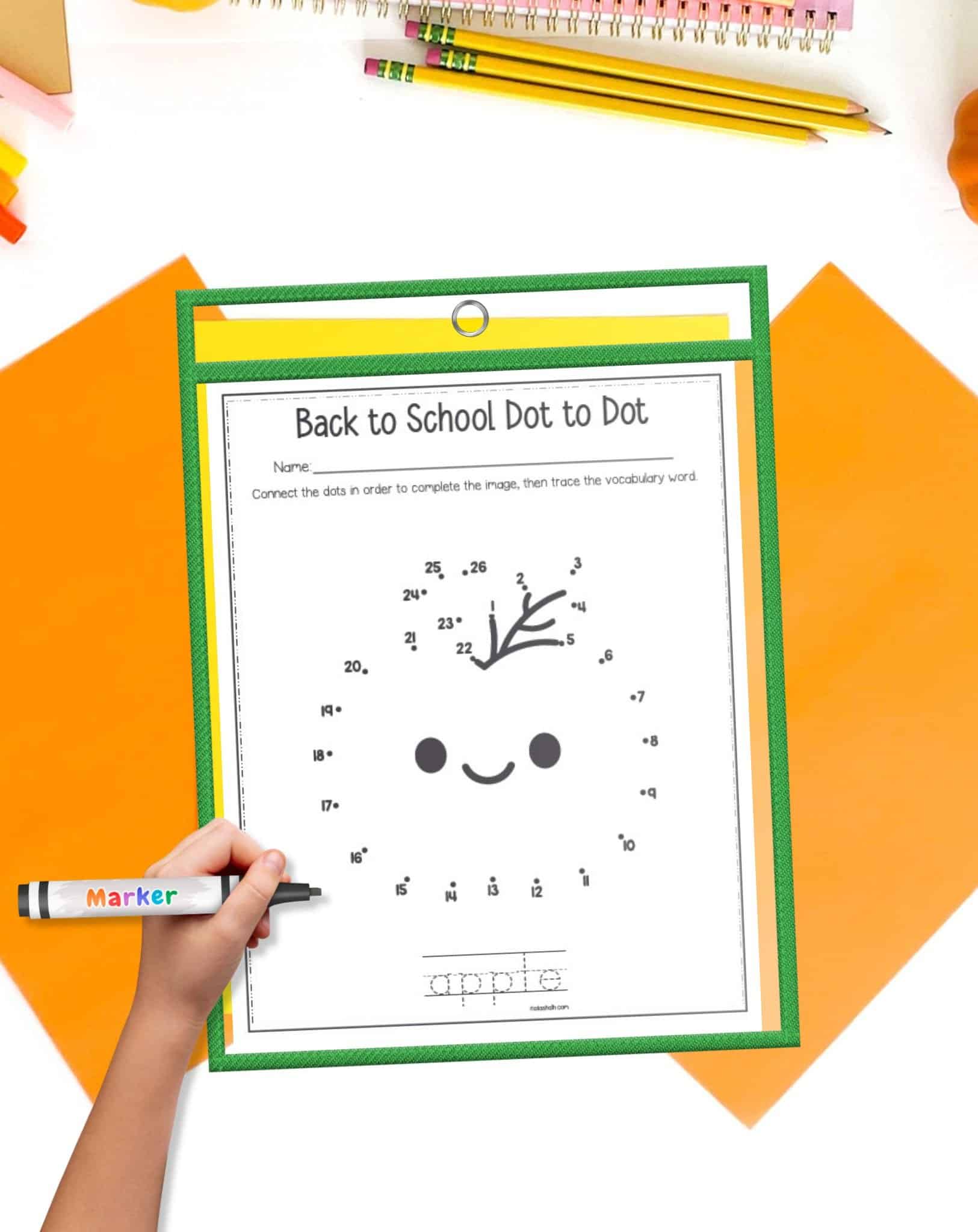 A top down image of an apple themed connect the dots worksheet in a dry erase pocket with a child's hand holding a marker