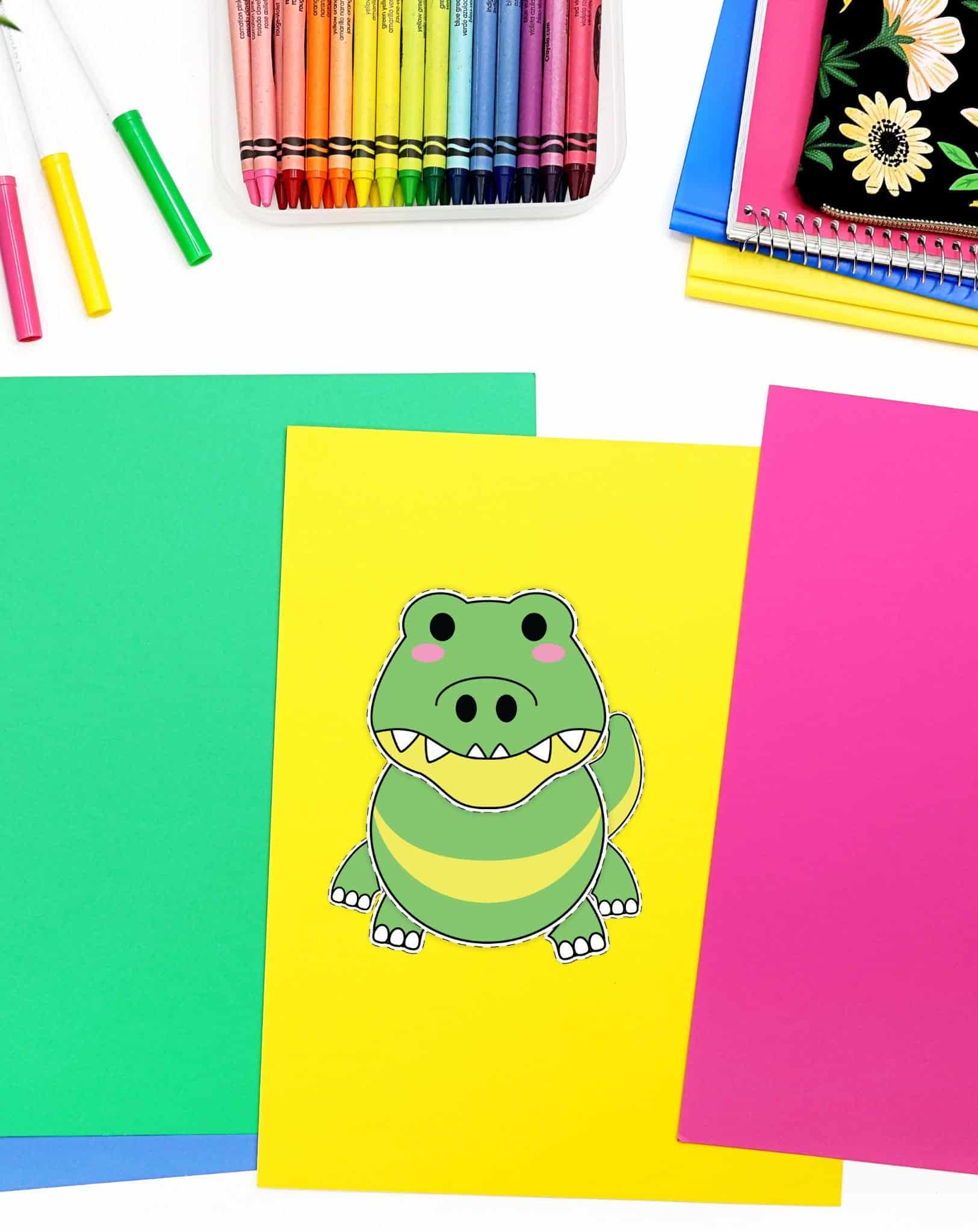 A completed cut and paste alligator craft on a desk with colorful papers and crayons