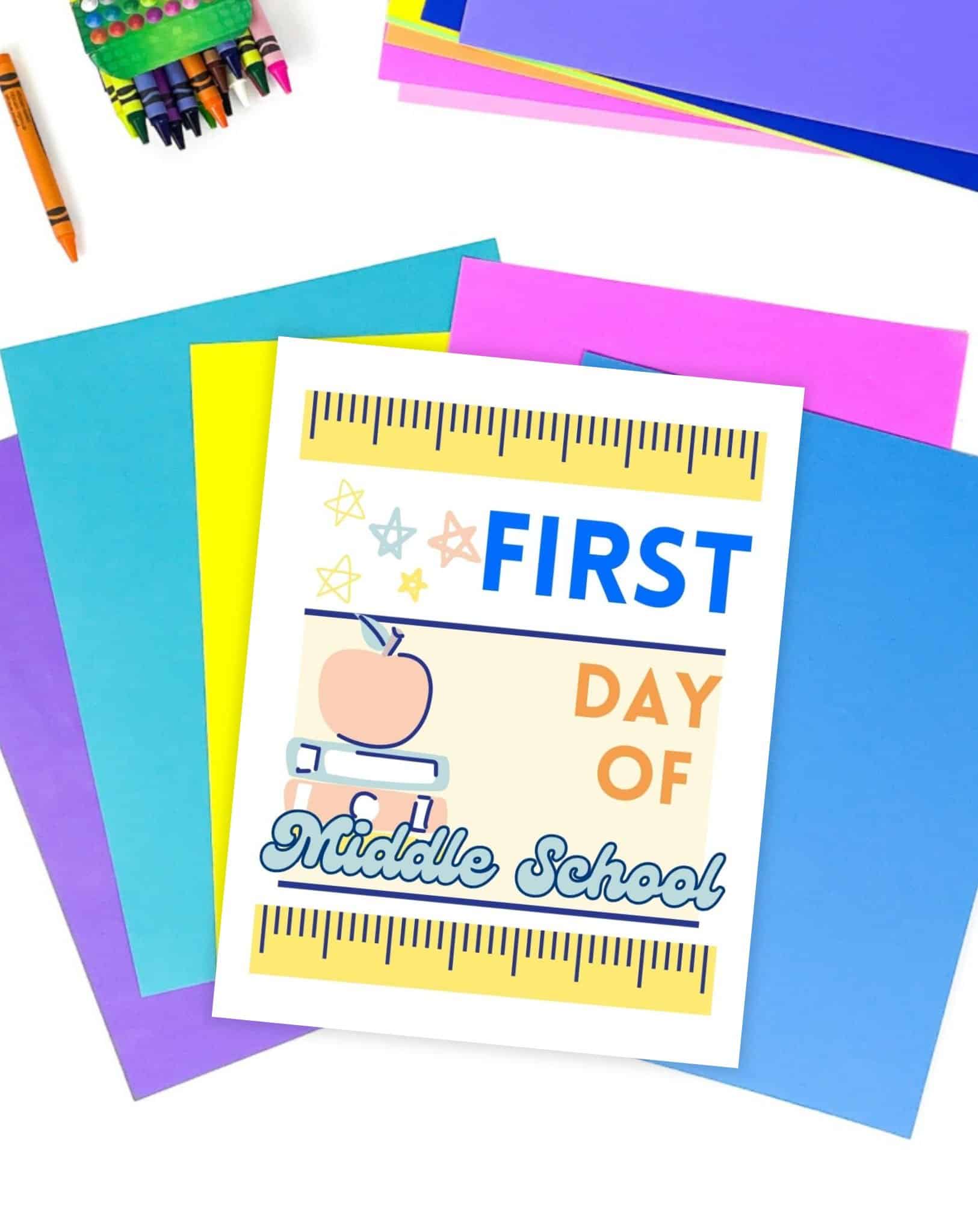 A first day of middle school sign on a desk with brightly colored paper and crayons