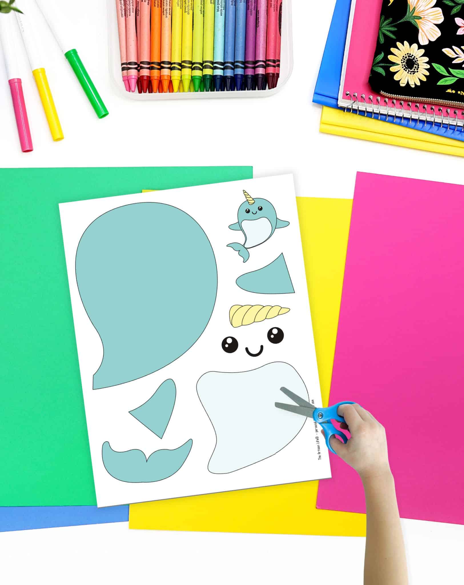 A top down image of a cut and pate narwhal craft on a desk with colorful school supplies