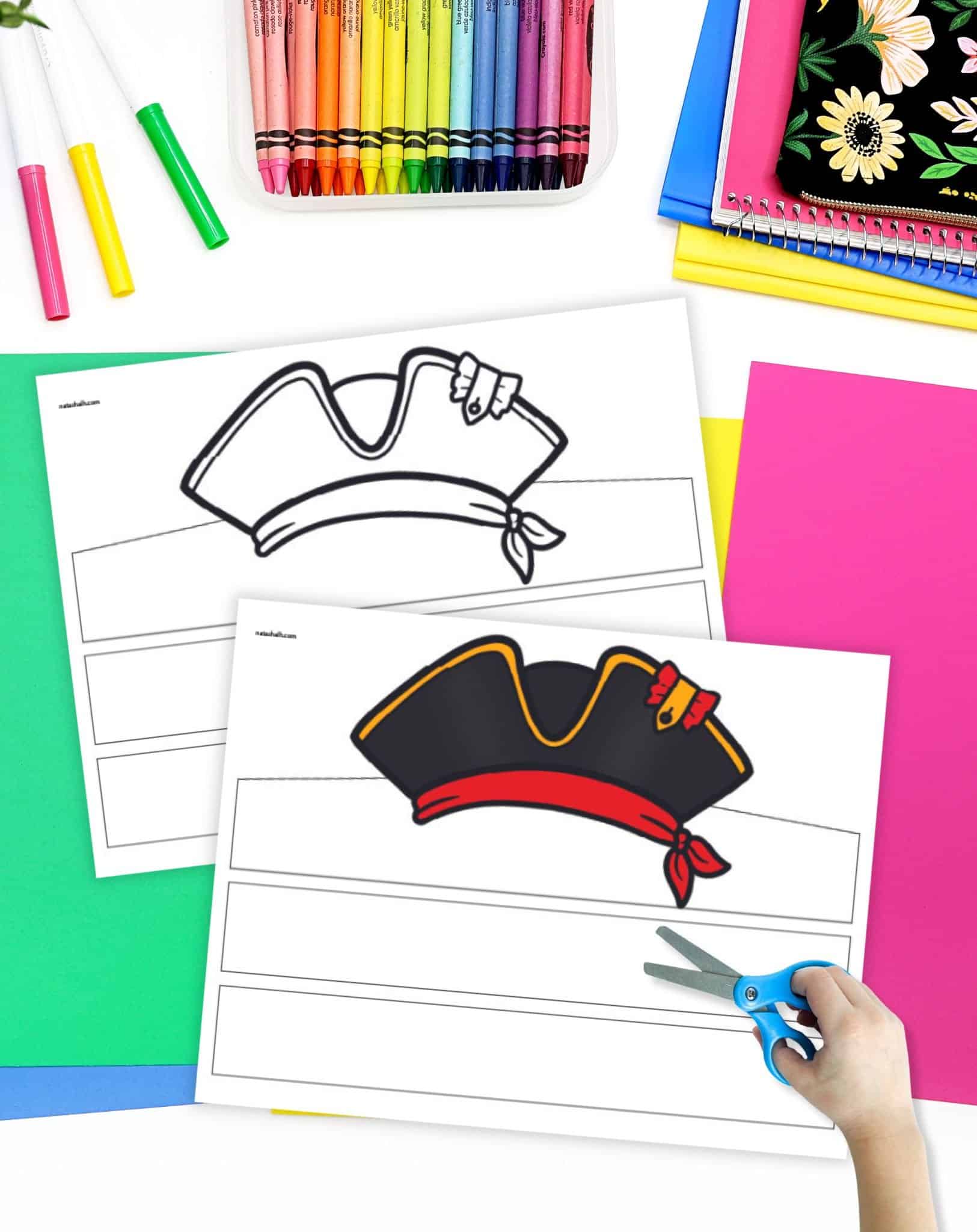 A preview of two printable pirate hat headbands on a desk with colorful papers and crayons