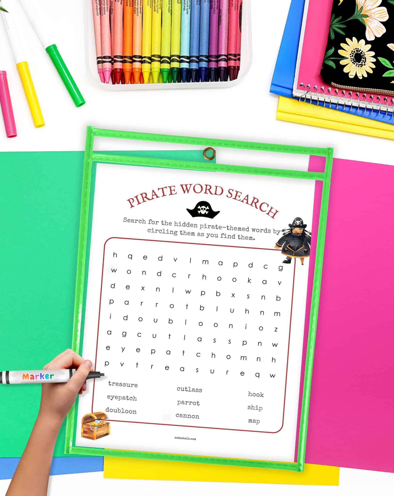 A pirate word search puzzle in a. green dry erase pocket on a desk with colorful papers and crayons