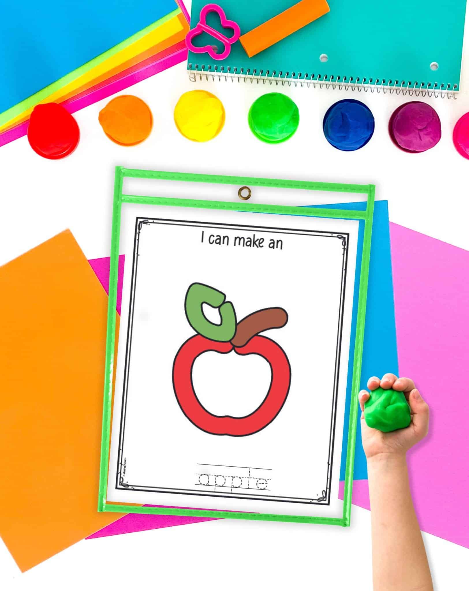 An apple themed play dough mat and a child's hand holding a ball of green play dough