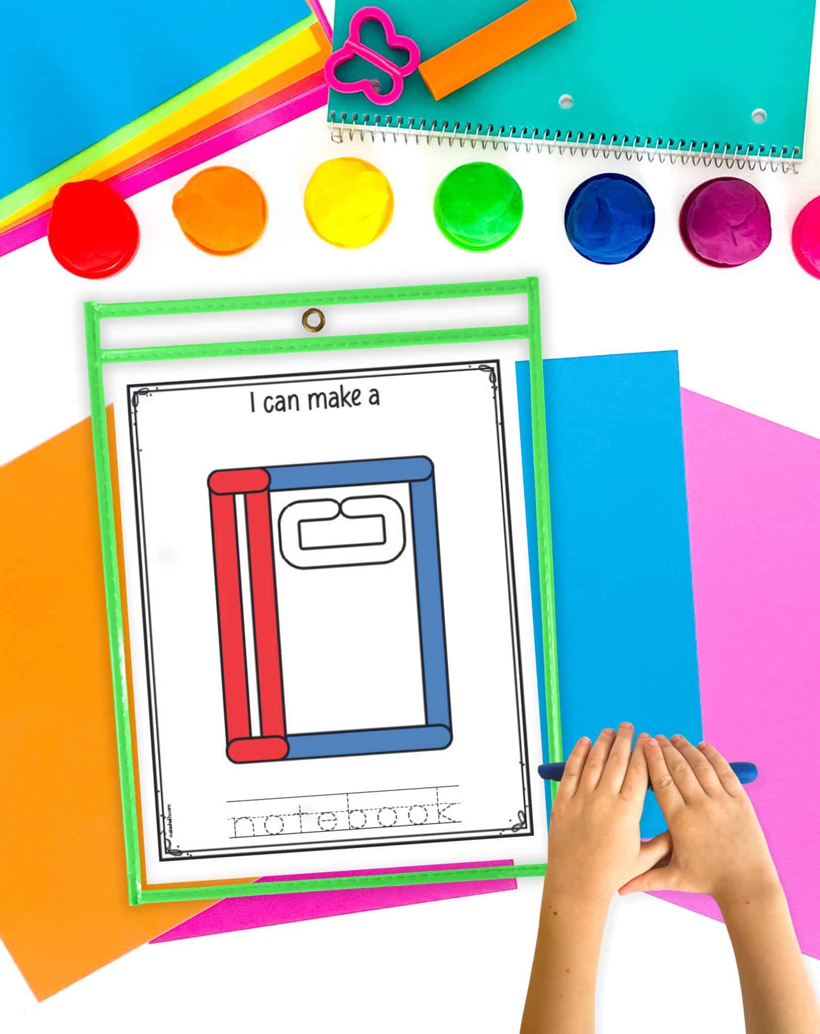 A notebook play dough mat in a green  dry erase pocket. A child's hands are rolling out a play dough snake on the desk.