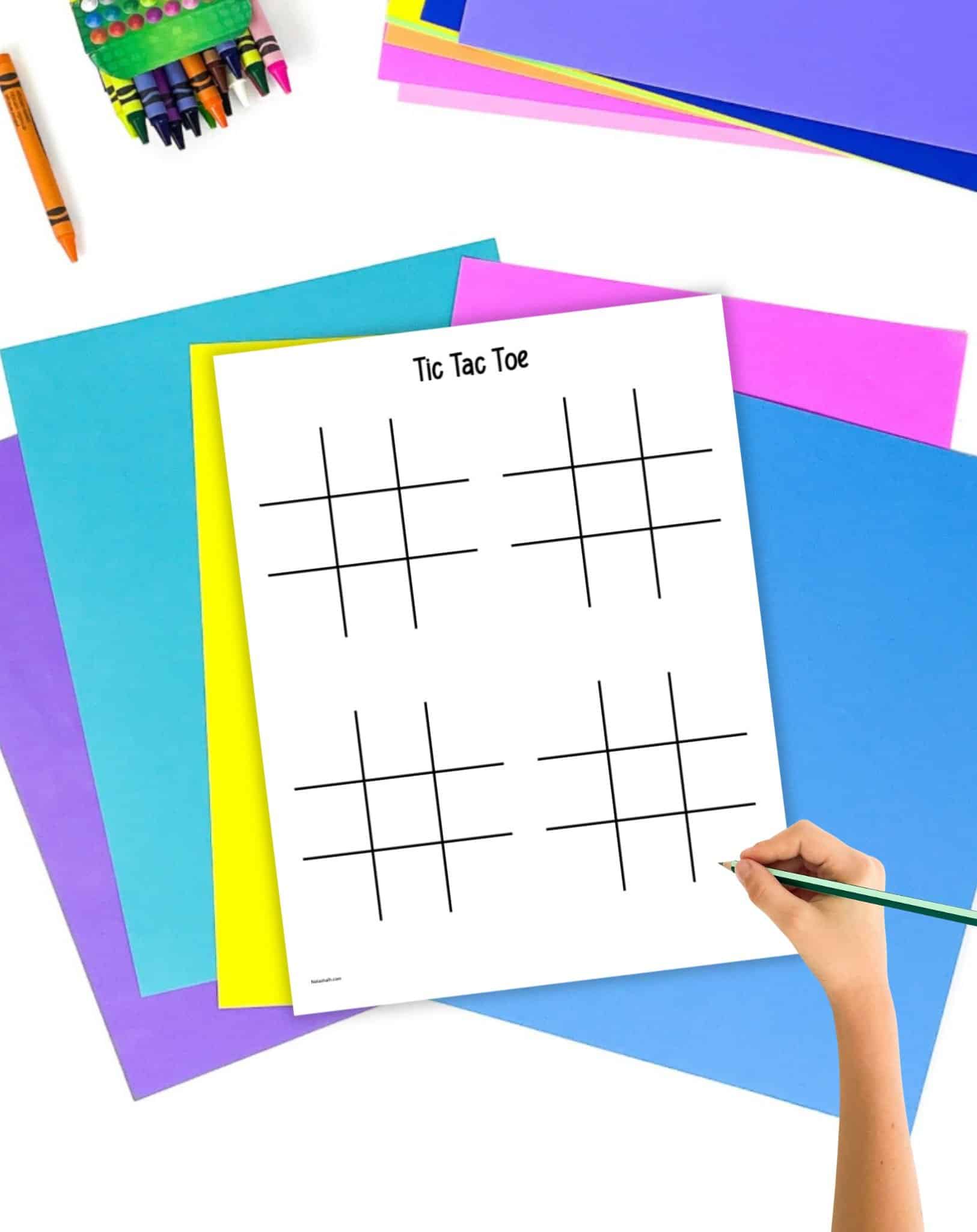 A hand with a pencil hovering over a printable with four blank tic tac toe boards