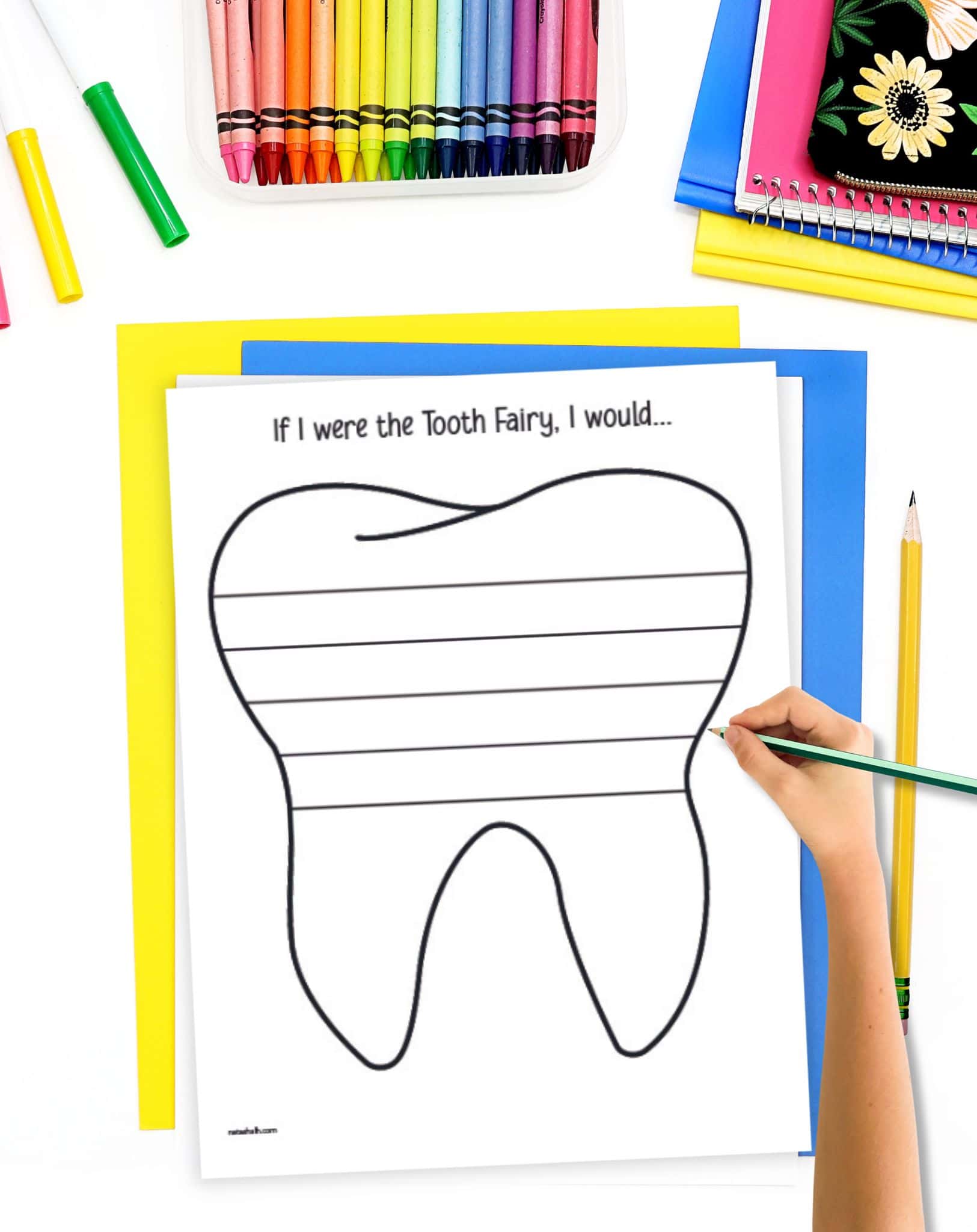 A child's hand holding a pencil over a tooth themed writing paper with a creative writing prompt