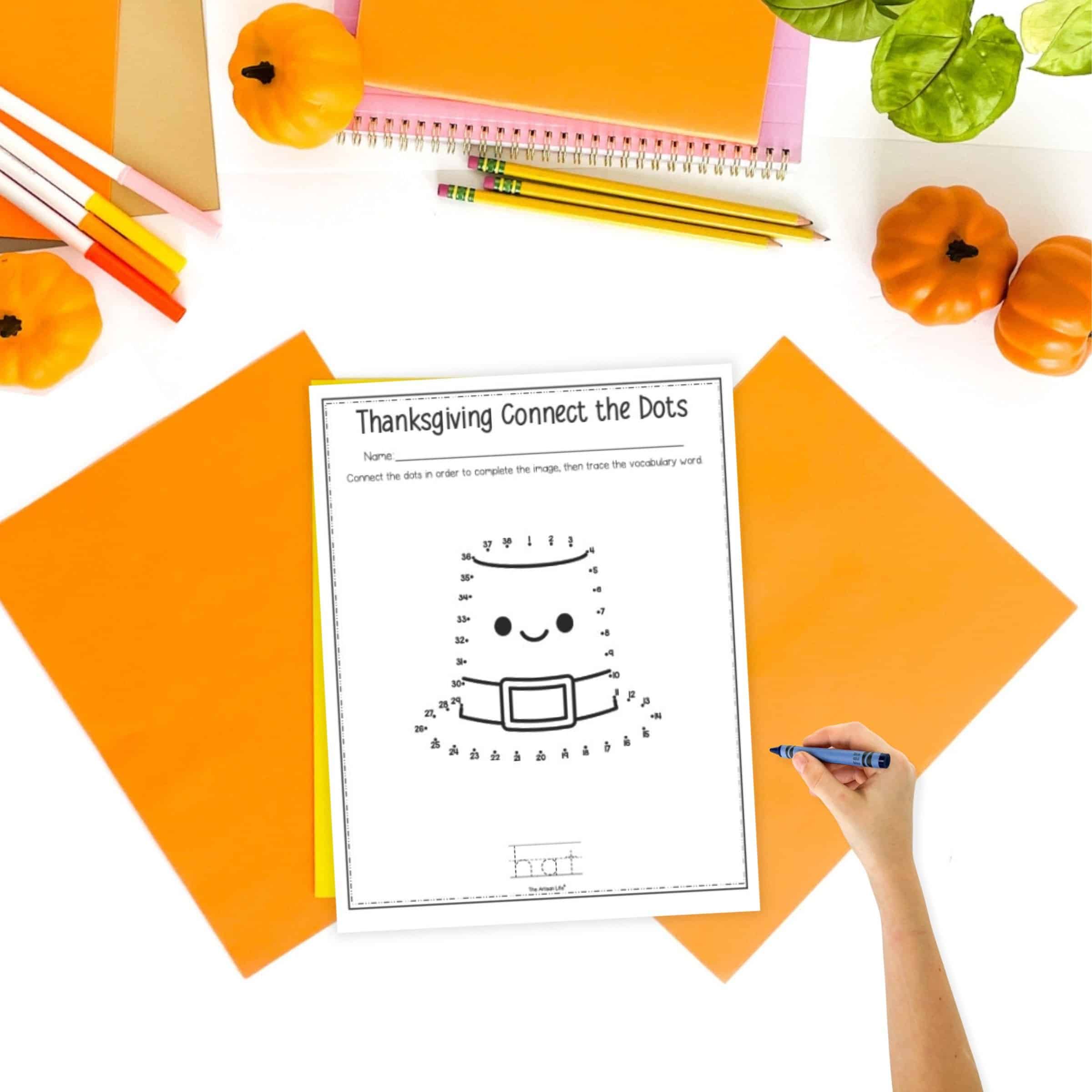 A top down image of a Pilgrim hat connect the dots image on a table with orange papers, pencils, and small pumpkins