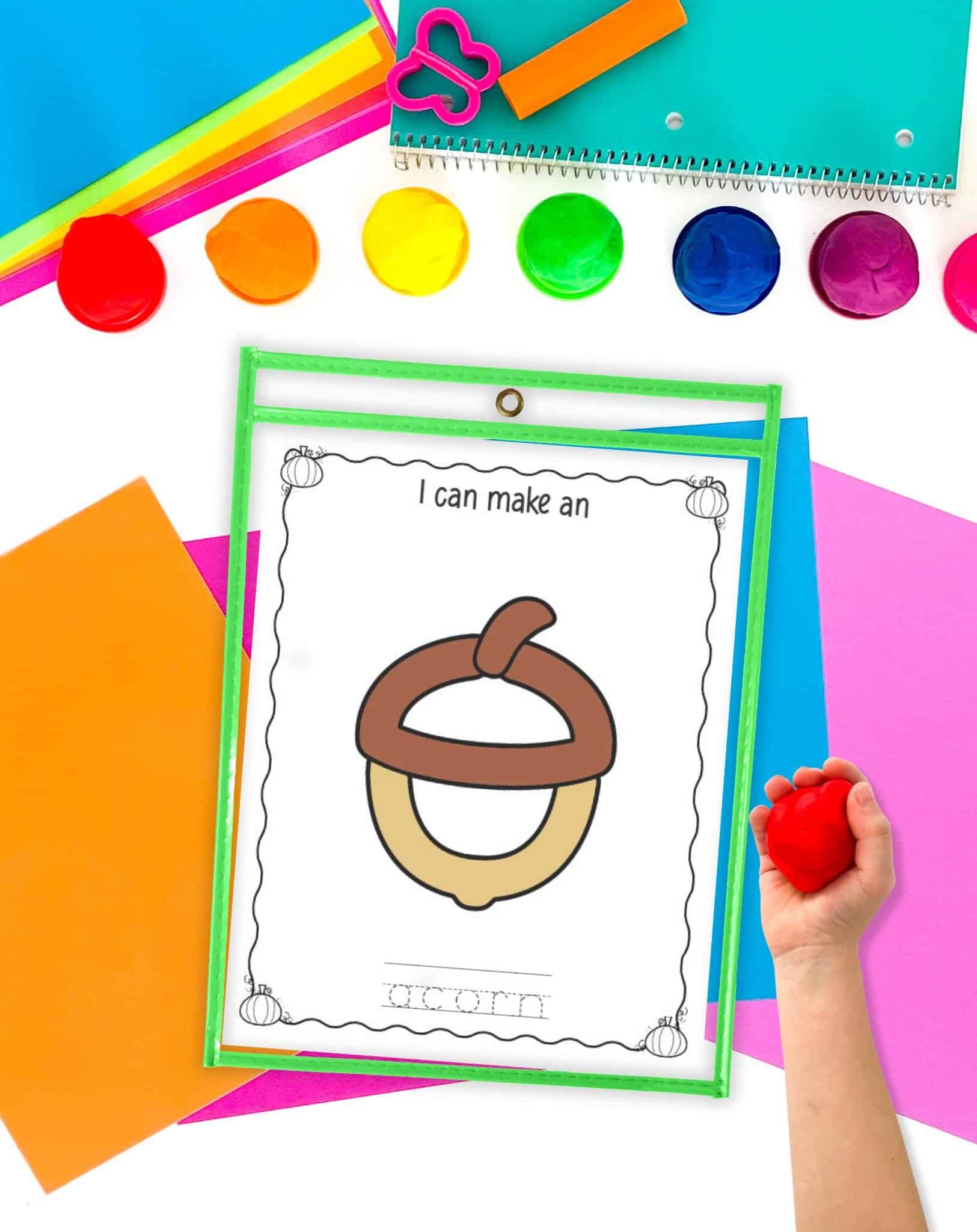 An acorn play dough mat in a dry erase pocket on a. table with colorful papers and play dough