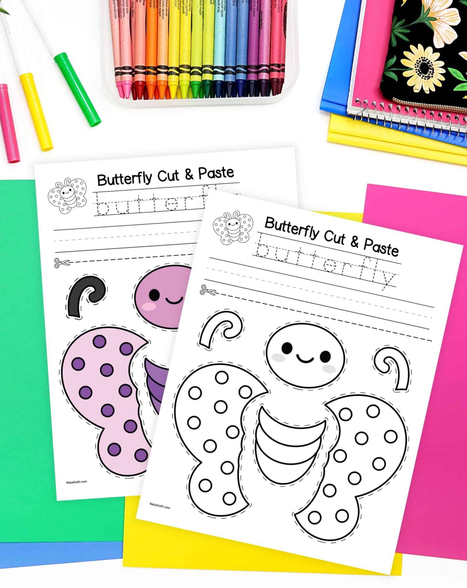 A top down image of two butterfly craft pages on a desk with colorful papers and crayons