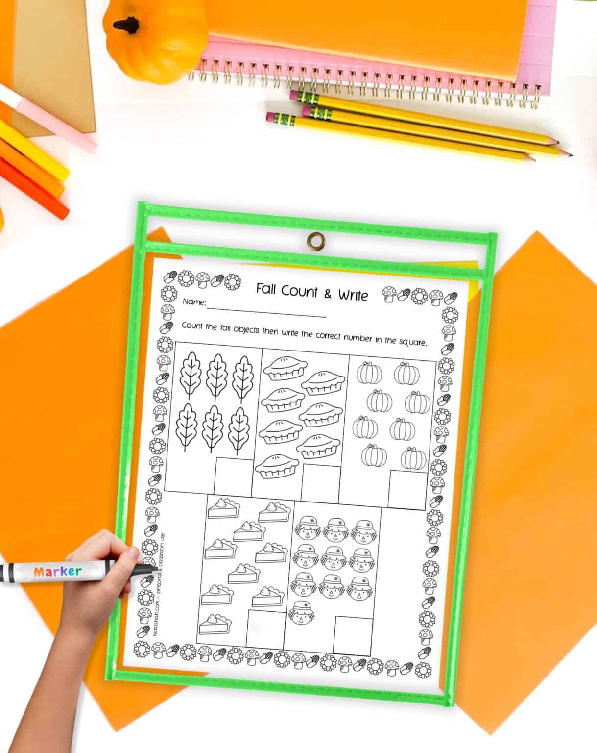 A fall count and write worksheet in a green dry erase pocket on a table with fall colored papers